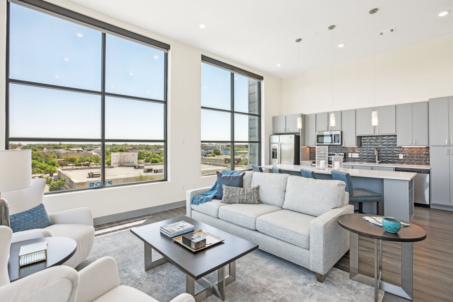 Penthouse living room with wraparound windows, a white sofa and an open kitchen beyond.