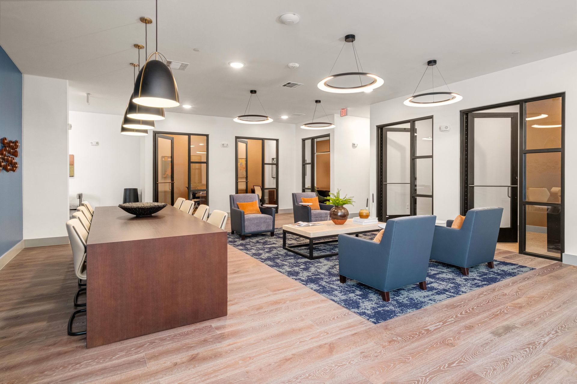 Modern apartment lounge at The Anderson: long table, chairs, comfy blue and gray armchairs on a rug. 
