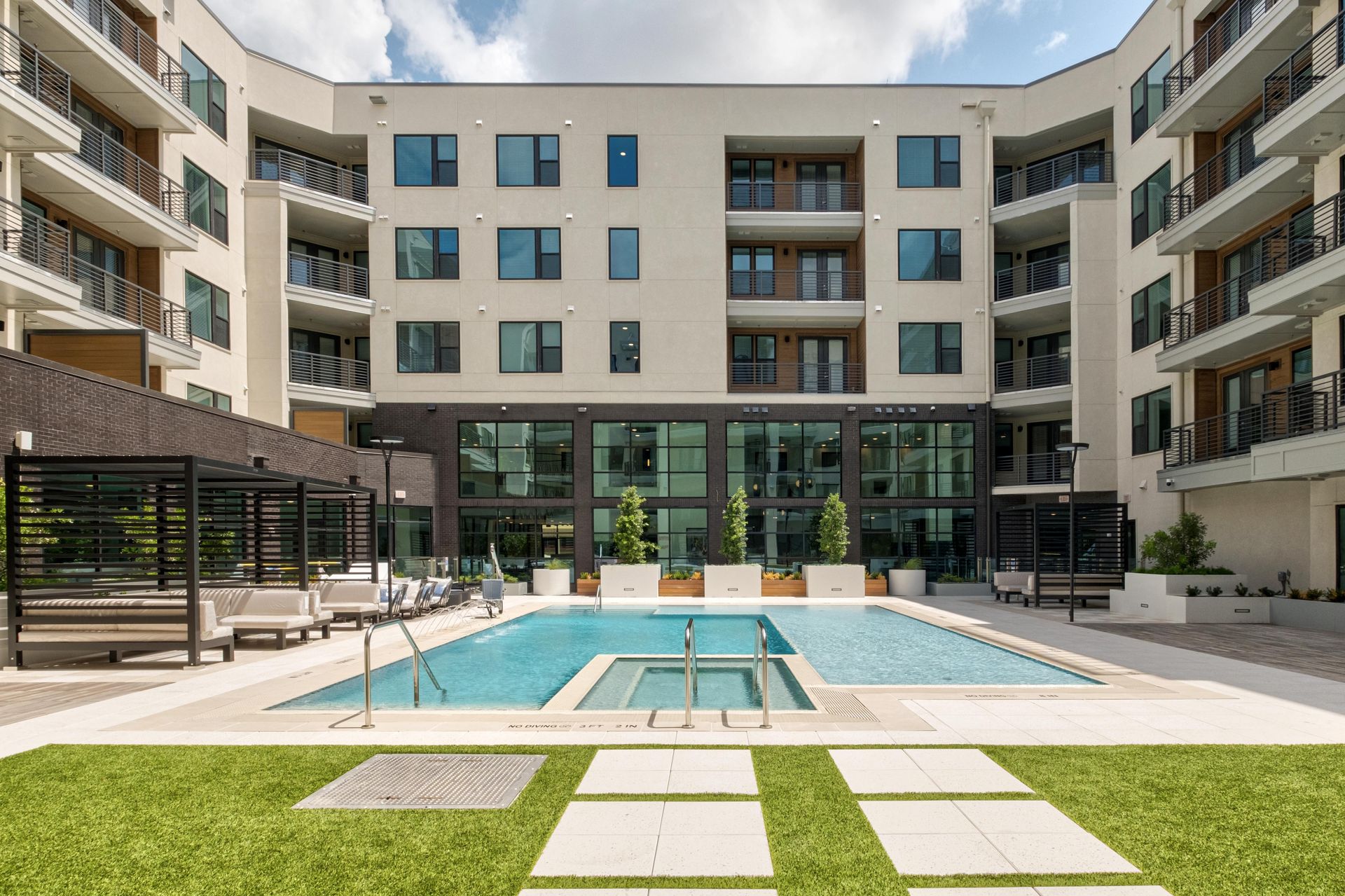 Courtyard pool with a lawn, paved walkways, cabanas and the curved building facade.
