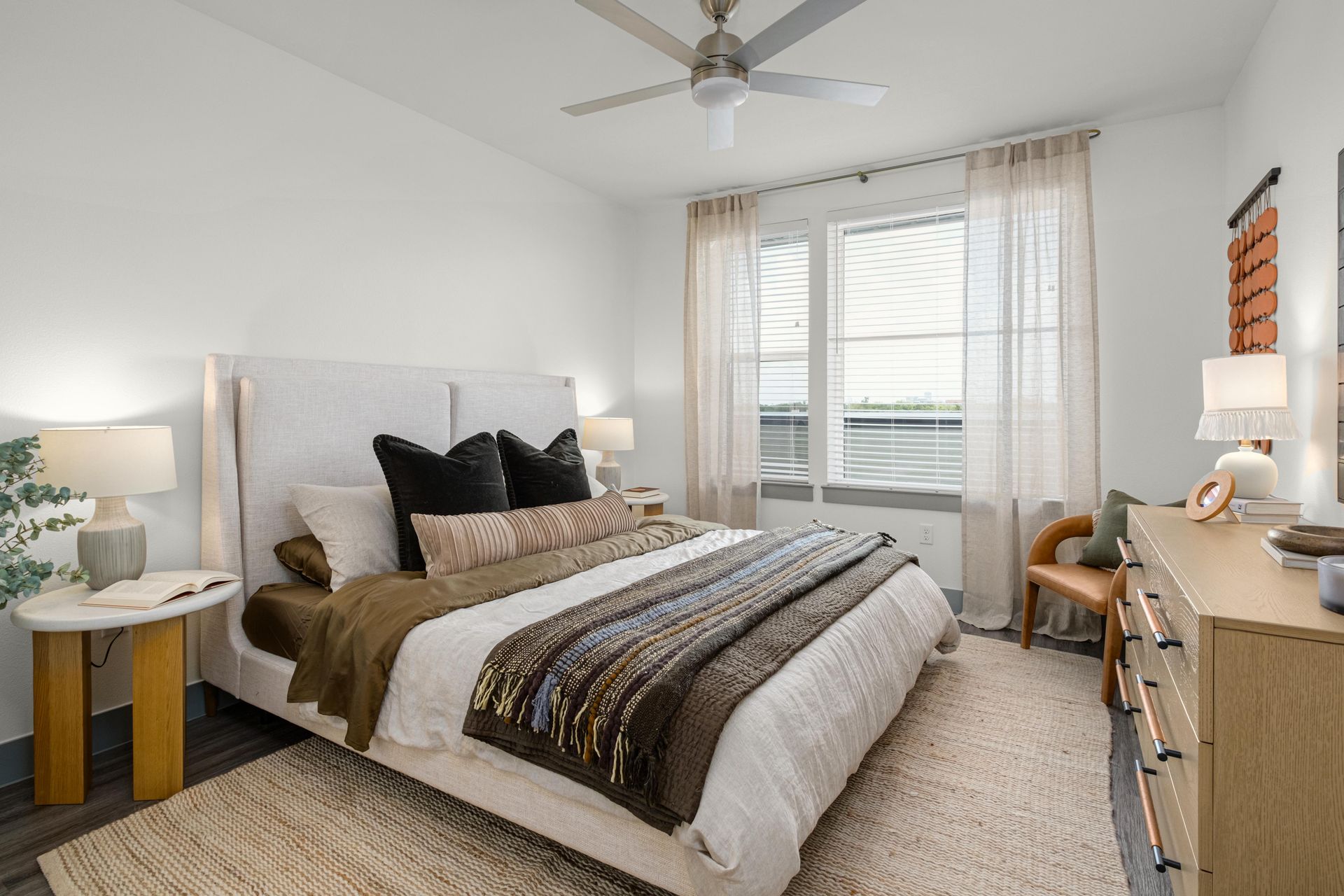 Bright, modern bedroom: light walls, dark floor, large bed. Window with blinds/curtains. 