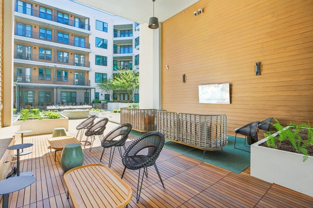 Outdoor lounge with a wood-panel wall, mounted television, swivel chairs and planter beds.