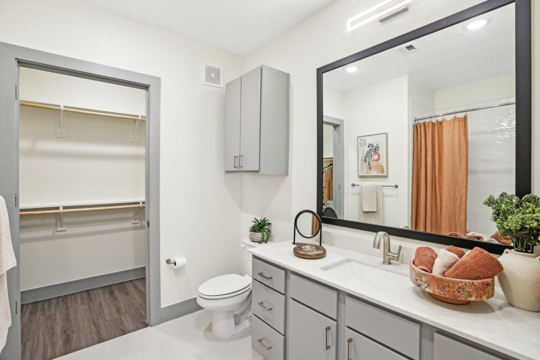 Bathroom vanity with a framed mirror, gray cabinets and an adjacent linen closet.