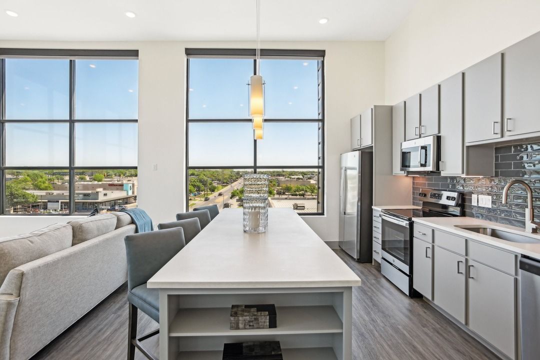 Penthouse kitchen with double-height windows, a long quartz island and stainless steel appliances.