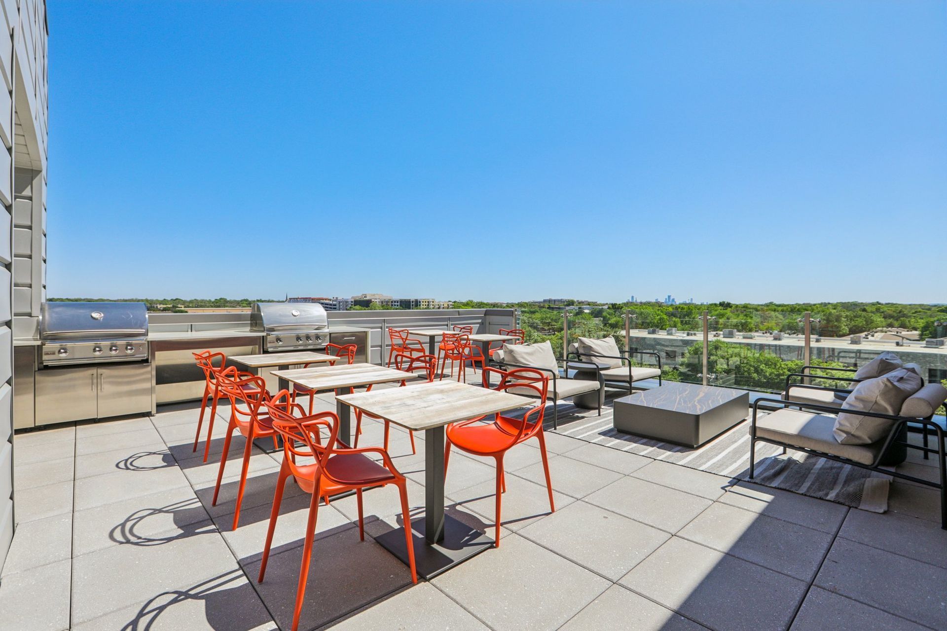 Rooftop grilling area with gas grills, orange dining chairs and open sky views.