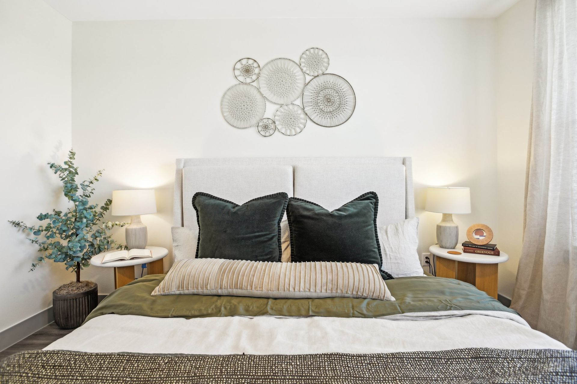 Bedroom with a white upholstered bed, olive bedding, matching nightstands and decorative wall plates.