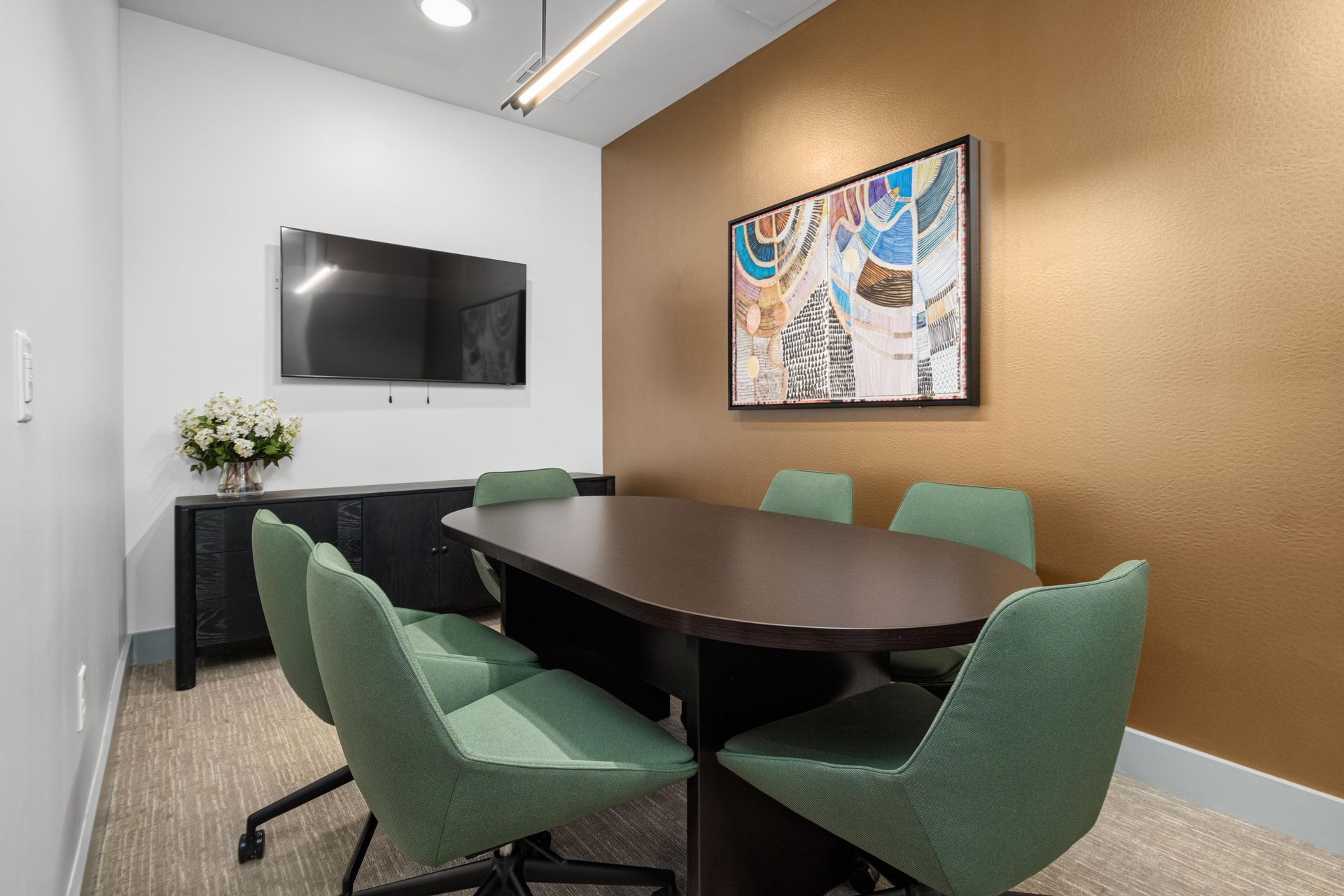 Private conference room with a dark oval table, green chairs and a wall-mounted screen.