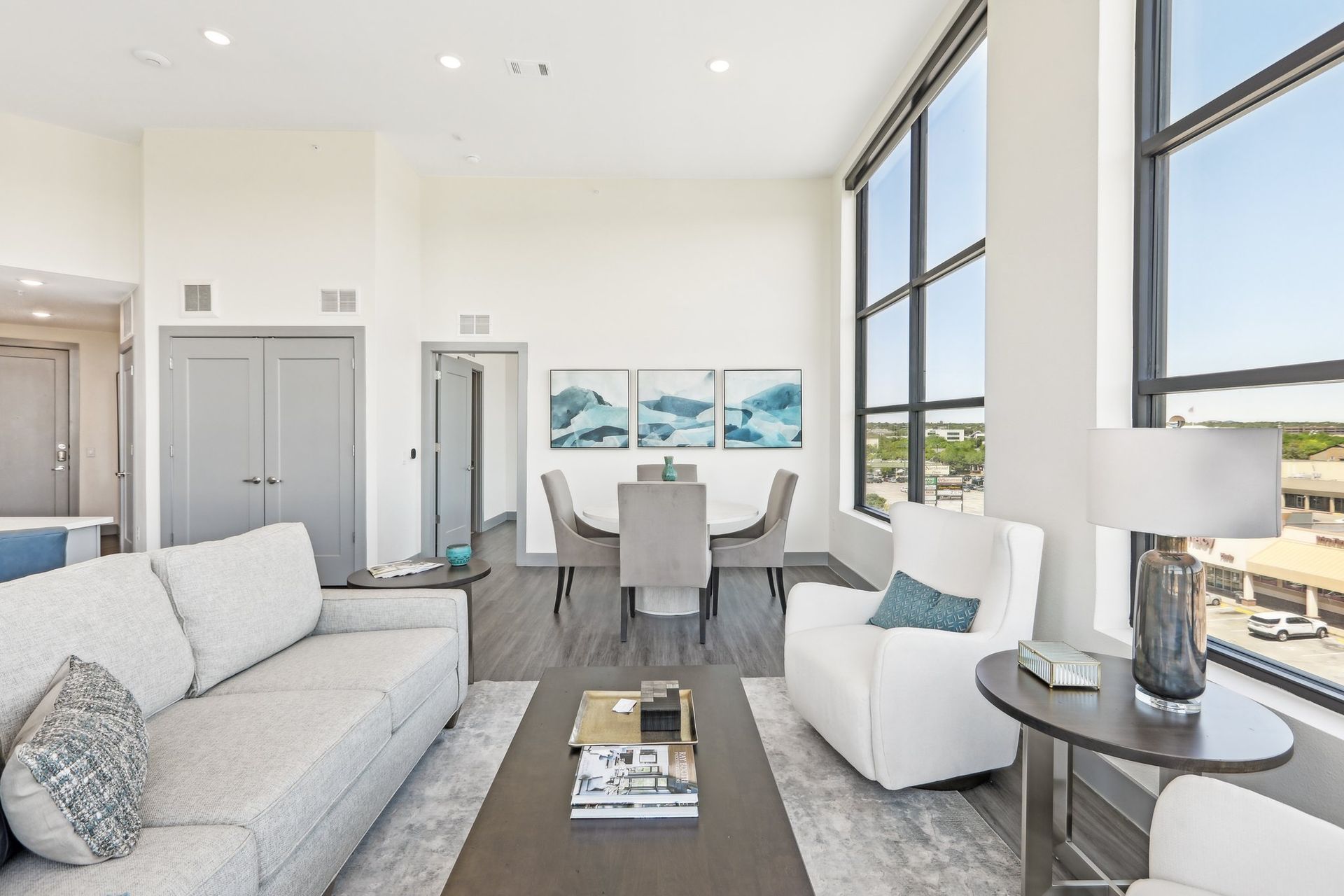Penthouse living area with a white sofa, swivel chairs and a dining table beside tall windows.