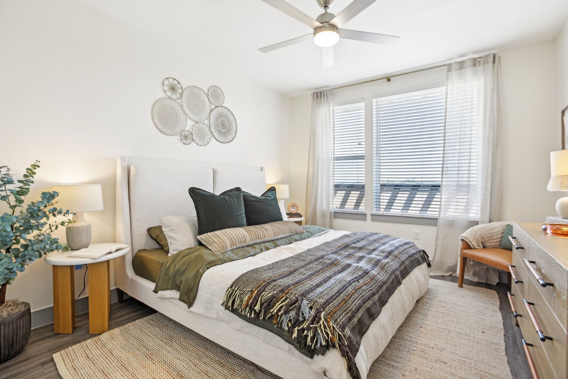 Bedroom with a ceiling fan, olive throw, bright window and a dresser along the wall.