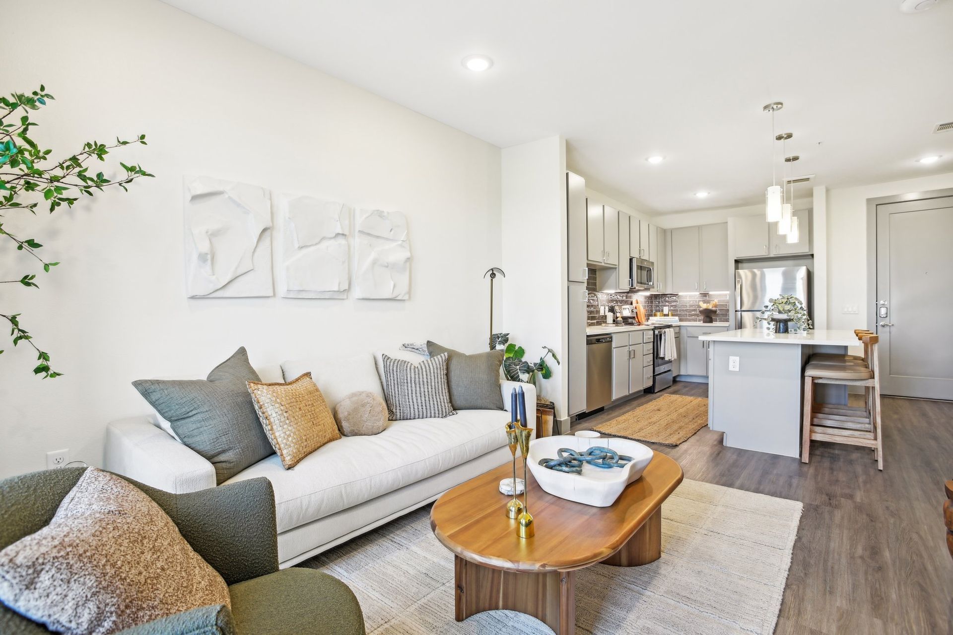 Bright living room with a sectional sofa, round wood coffee table and an open sightline to the kitchen.