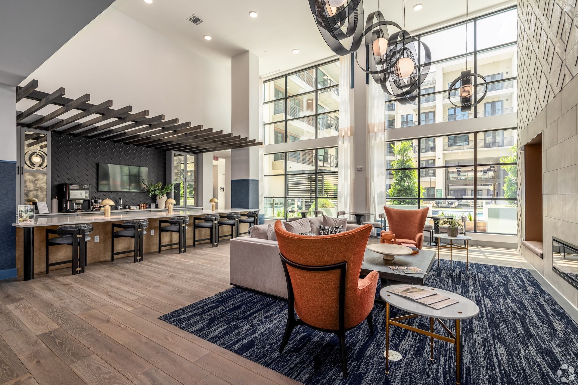 Clubhouse bar and lounge with orange accent chairs, high ceilings and a long communal counter.