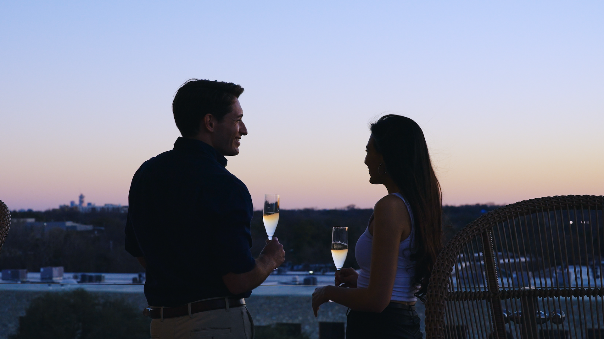 Two residents toasting on the sky deck at sunset with the Austin skyline behind.