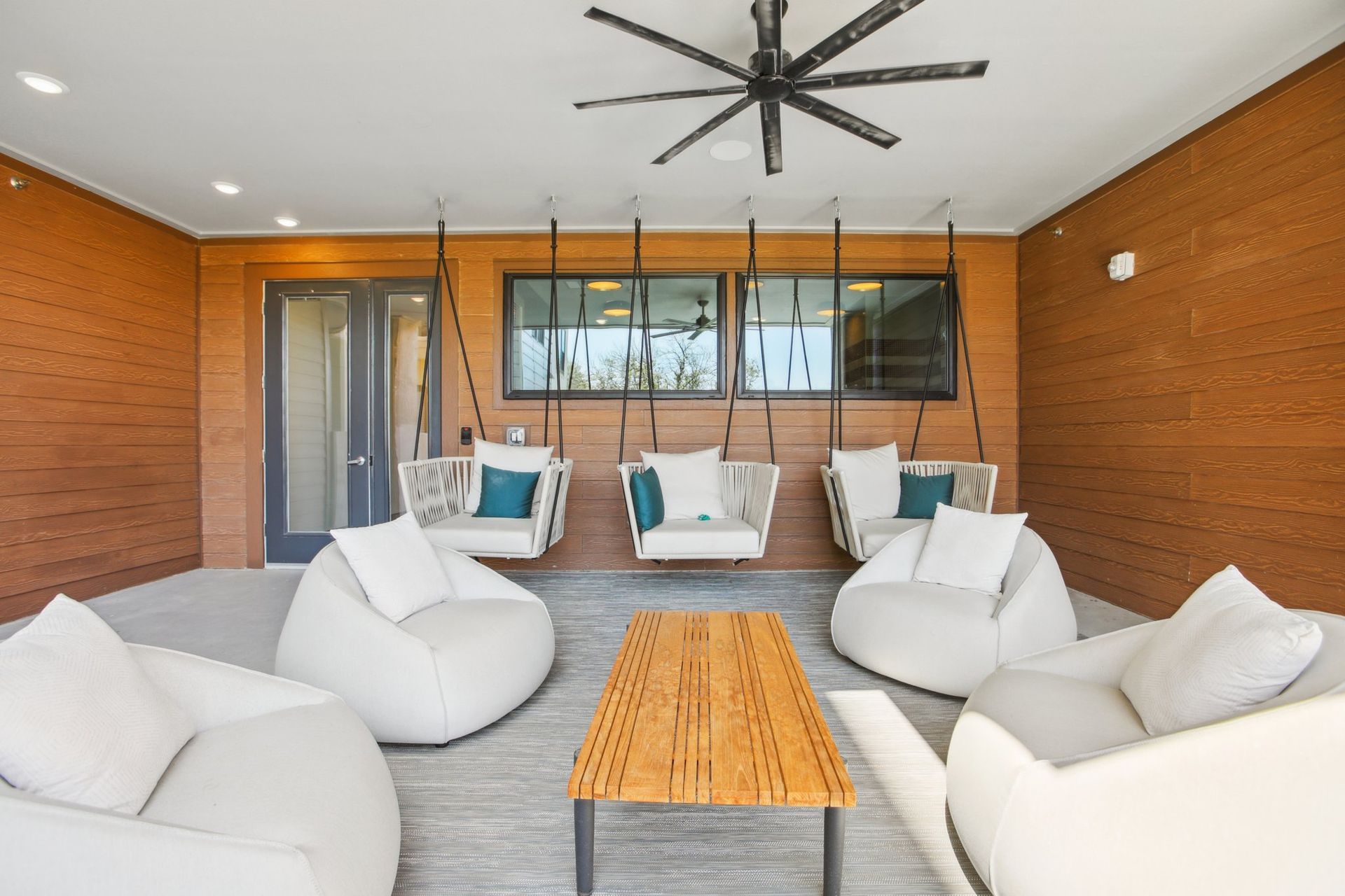 Covered outdoor lounge with hanging swing chairs, bean bag seating and a wood ceiling fan.