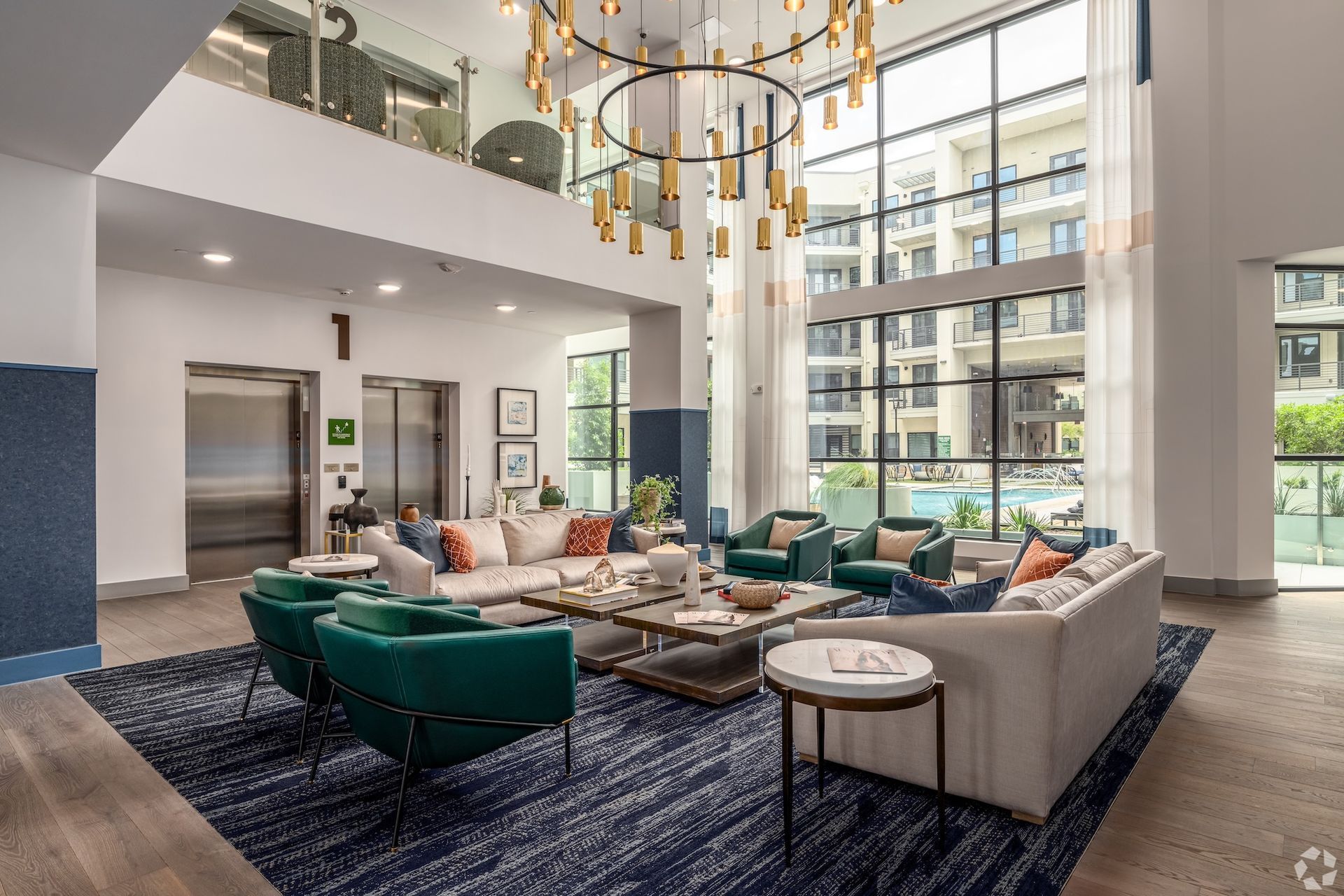 Two-story clubhouse lounge with teal armchairs, a patterned rug and a gold chandelier.