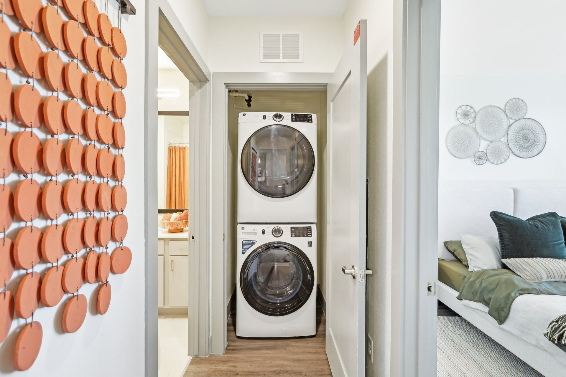 Stacked washer and dryer in a bedroom hallway closet beside an orange textured wall installation.