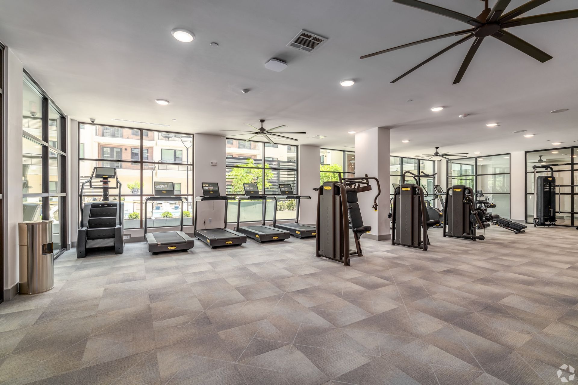 Fitness center with cardio machines, strength equipment and a wall of windows facing the pool.