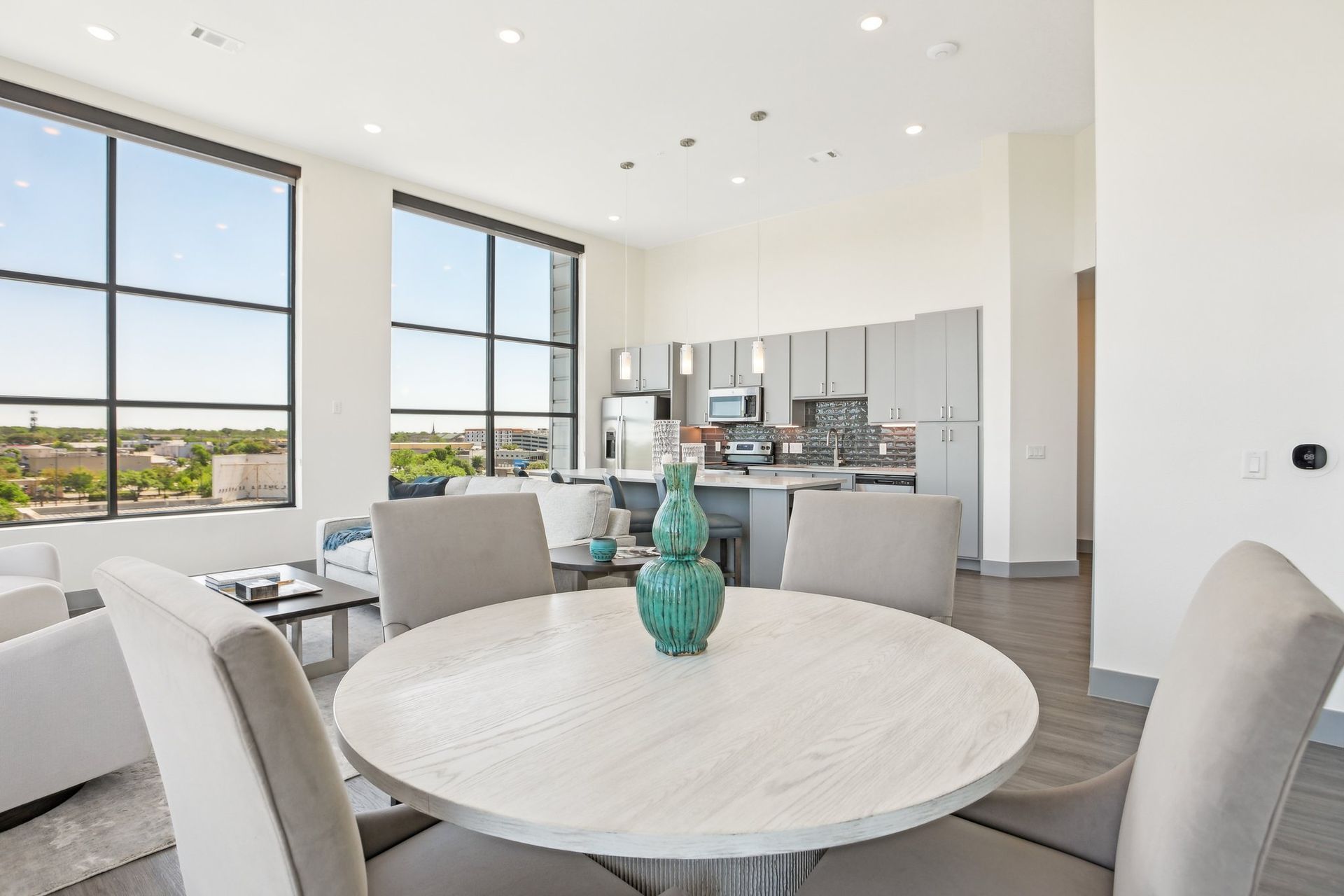 Penthouse dining table for six with an open kitchen and panoramic windows behind.