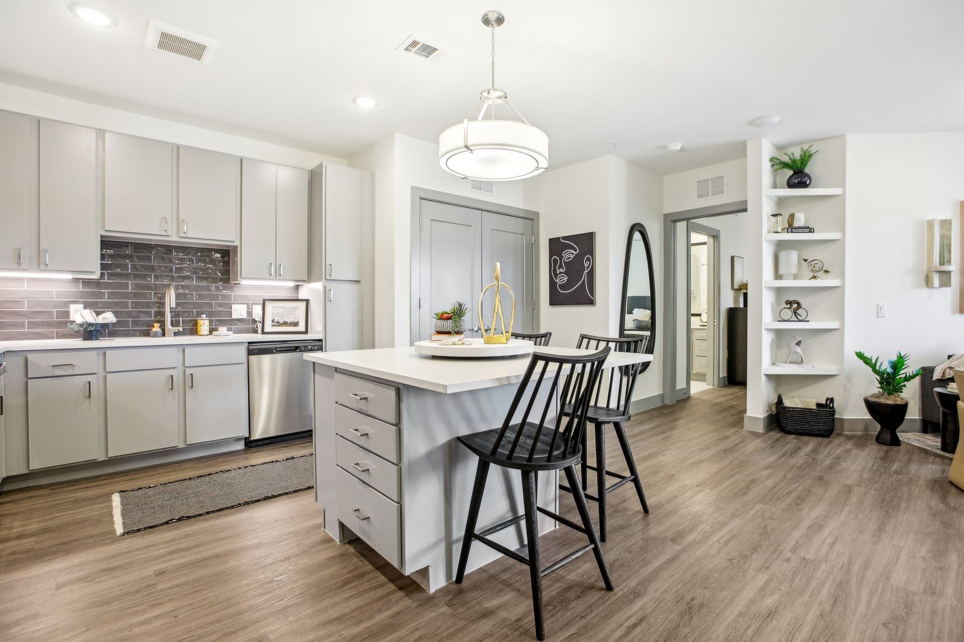 Galley kitchen with a quartz island, pendant lighting, stainless appliances and open shelving beyond.