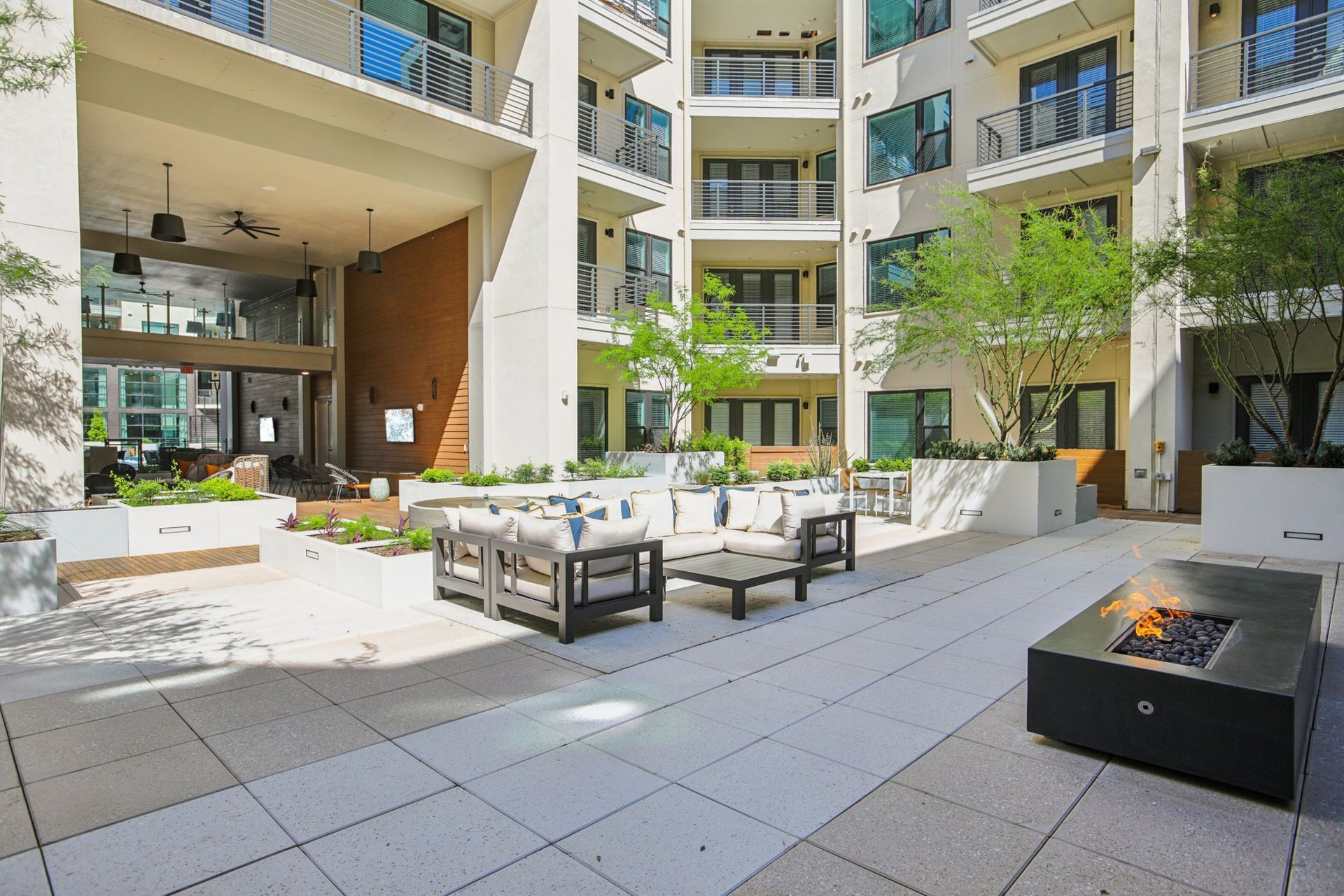 Courtyard seating area with sofas, a lit gas fire pit and shade trees.