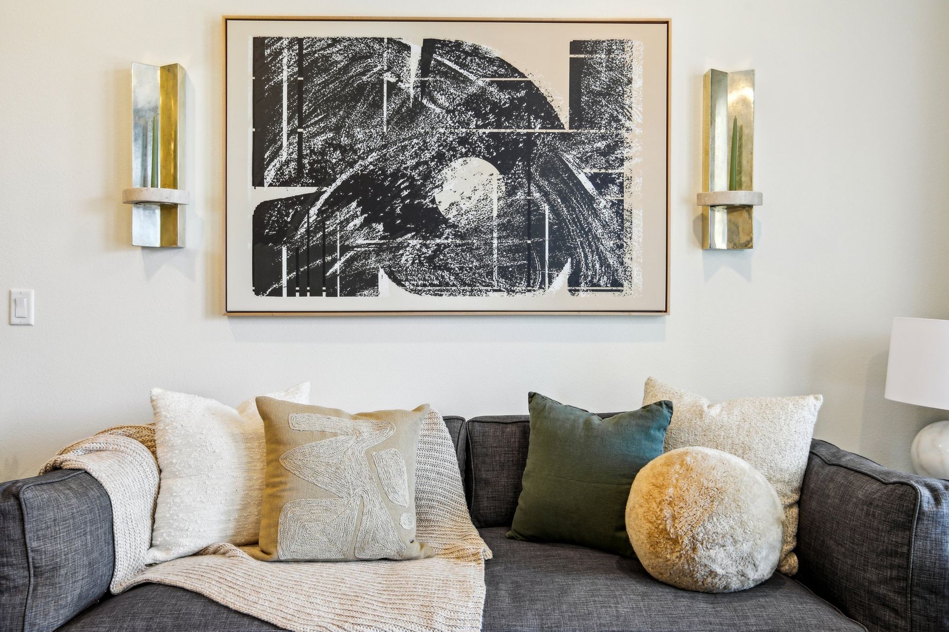 Sectional sofa layered with neutral and mustard cushions beneath a large framed black and white artwork.
