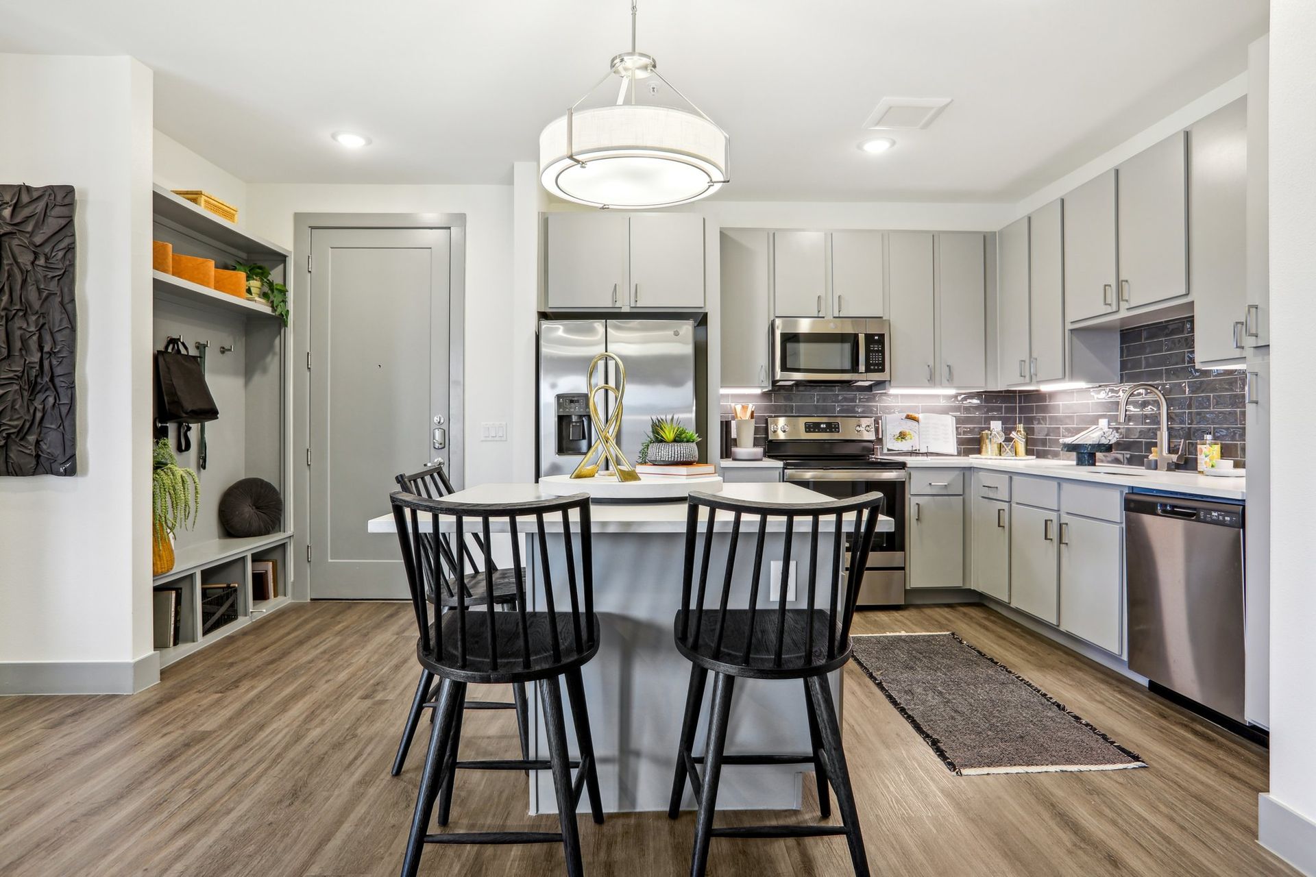 Kitchen with gray shaker cabinets, stainless steel appliances, tile backsplash and an island with black bar stools.