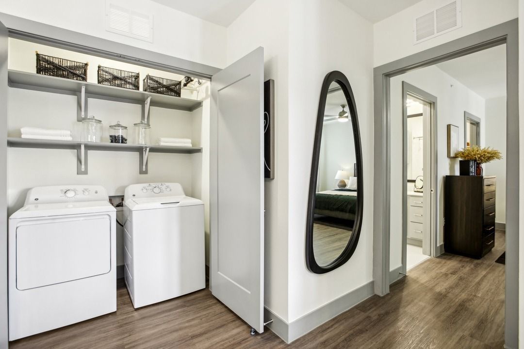 Full-size side-by-side washer and dryer in a hallway laundry nook with wire shelving.