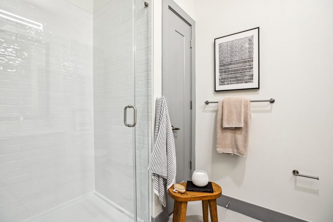 Glass-enclosed shower with white subway tile, a wood stool and a chrome towel bar.