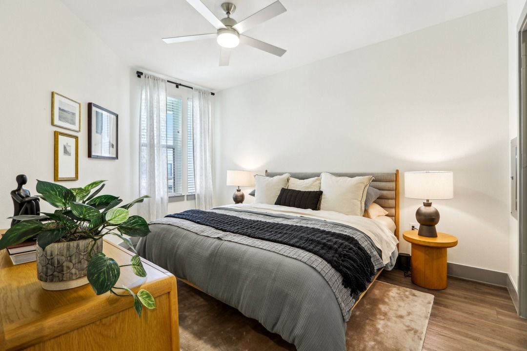 Bedroom with a ceiling fan, upholstered headboard, wood nightstands and a potted plant by the window.