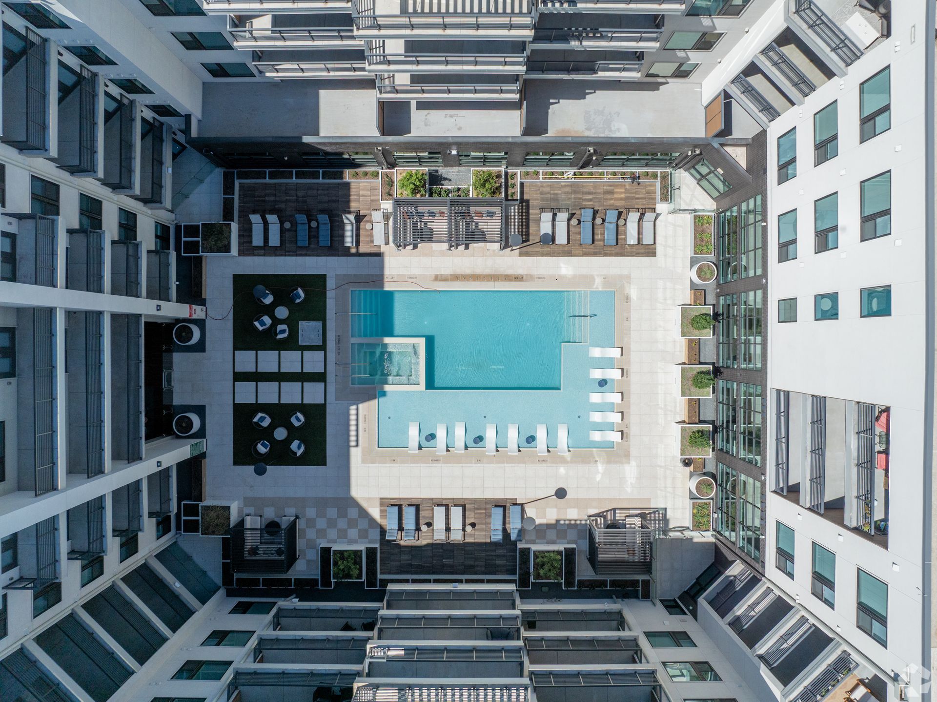 Overhead view of a modern apartment complex courtyard with a pool, lounge chairs, and green spaces.