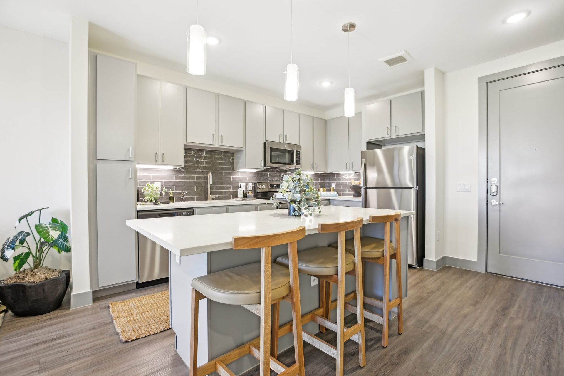 Modern kitchen with island, gray cabinets, stainless steel appliances, and wood bar stools.