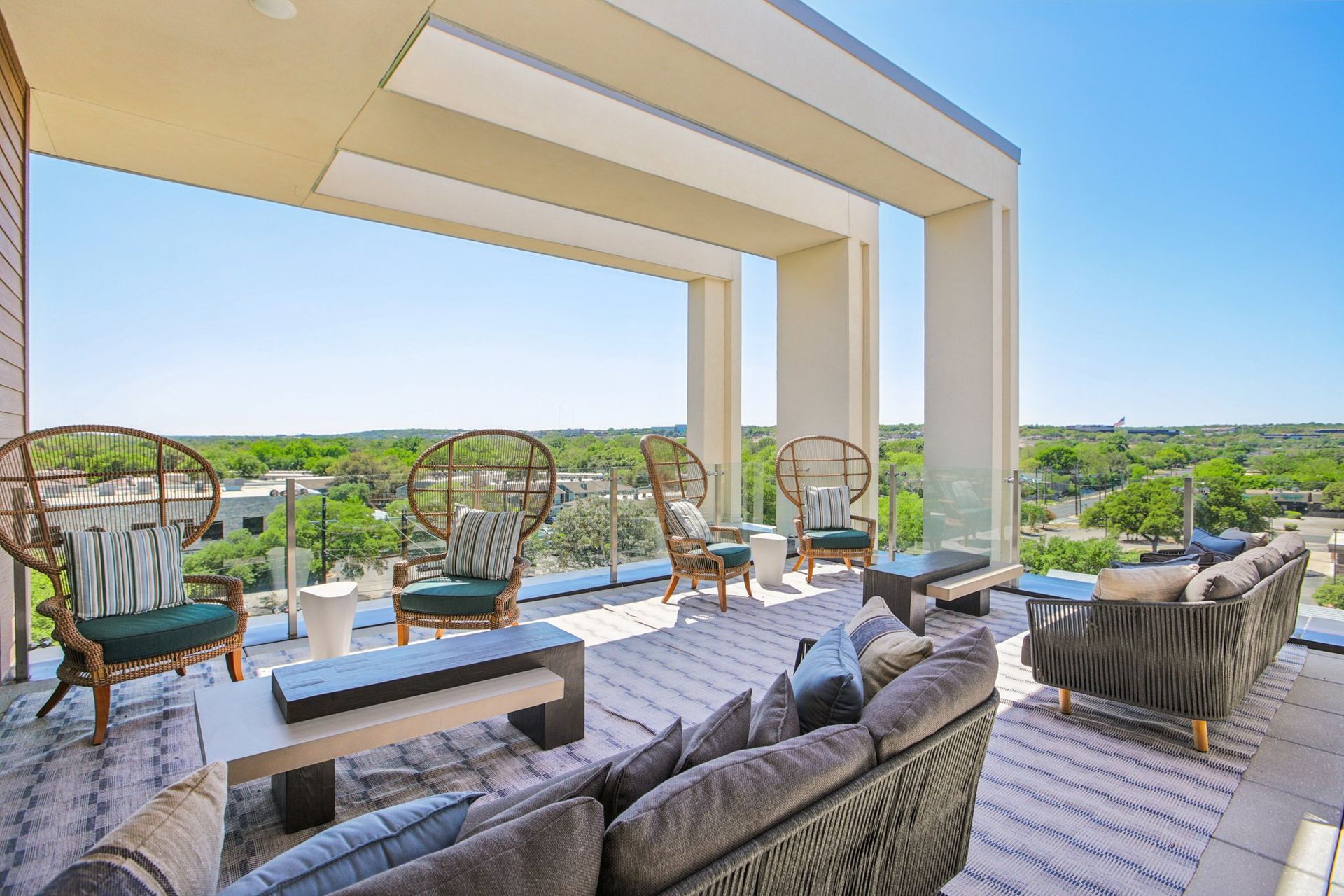 Spacious outdoor patio with modern furniture, including couches and wicker chairs, overlooking a cityscape on a sunny day.