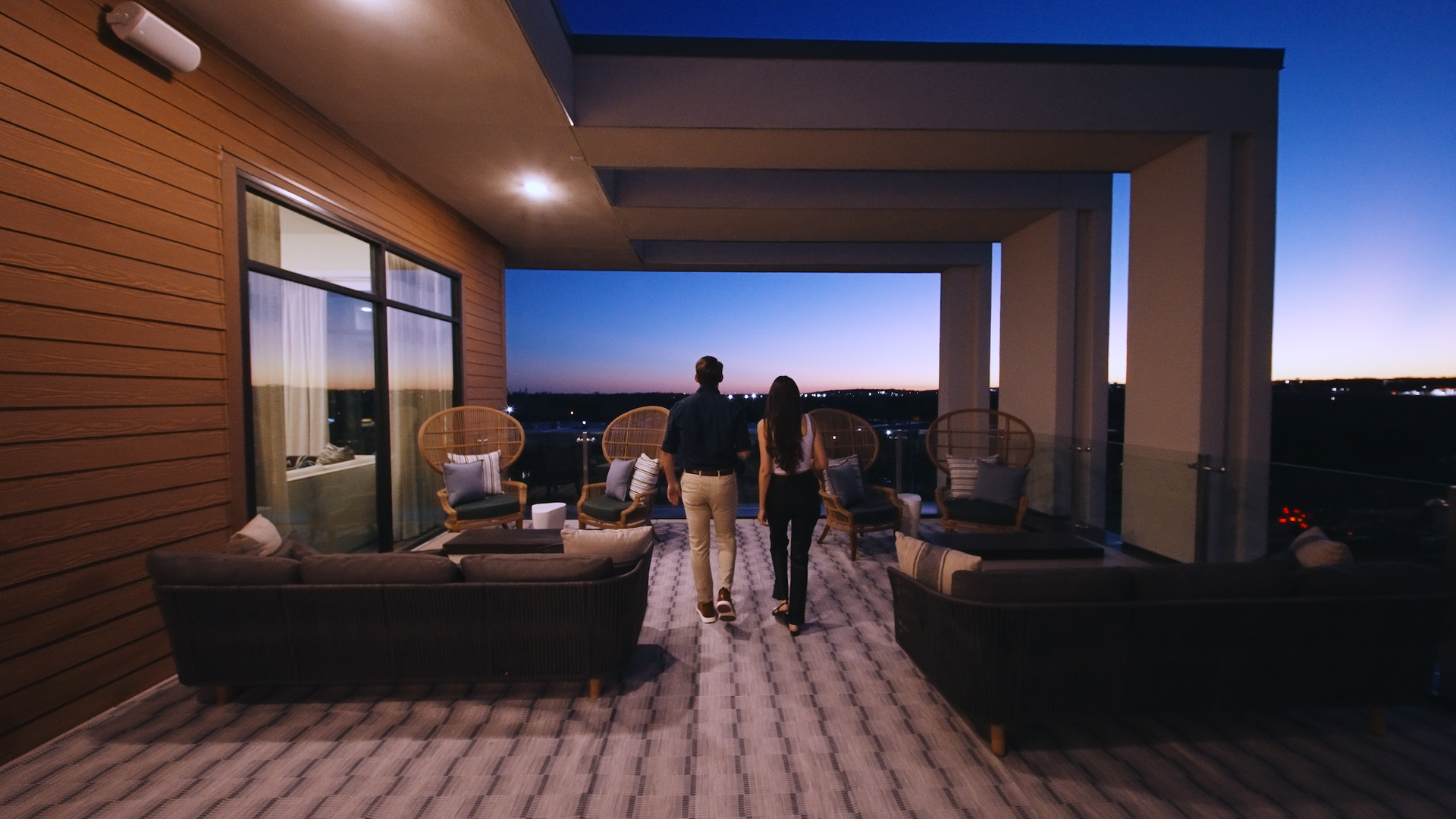 Residents on the sky deck at dusk with lounge seating and city lights beyond.