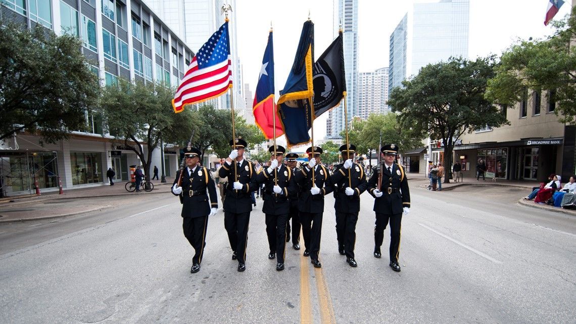 A marching band in uniform carries flags down a city street.