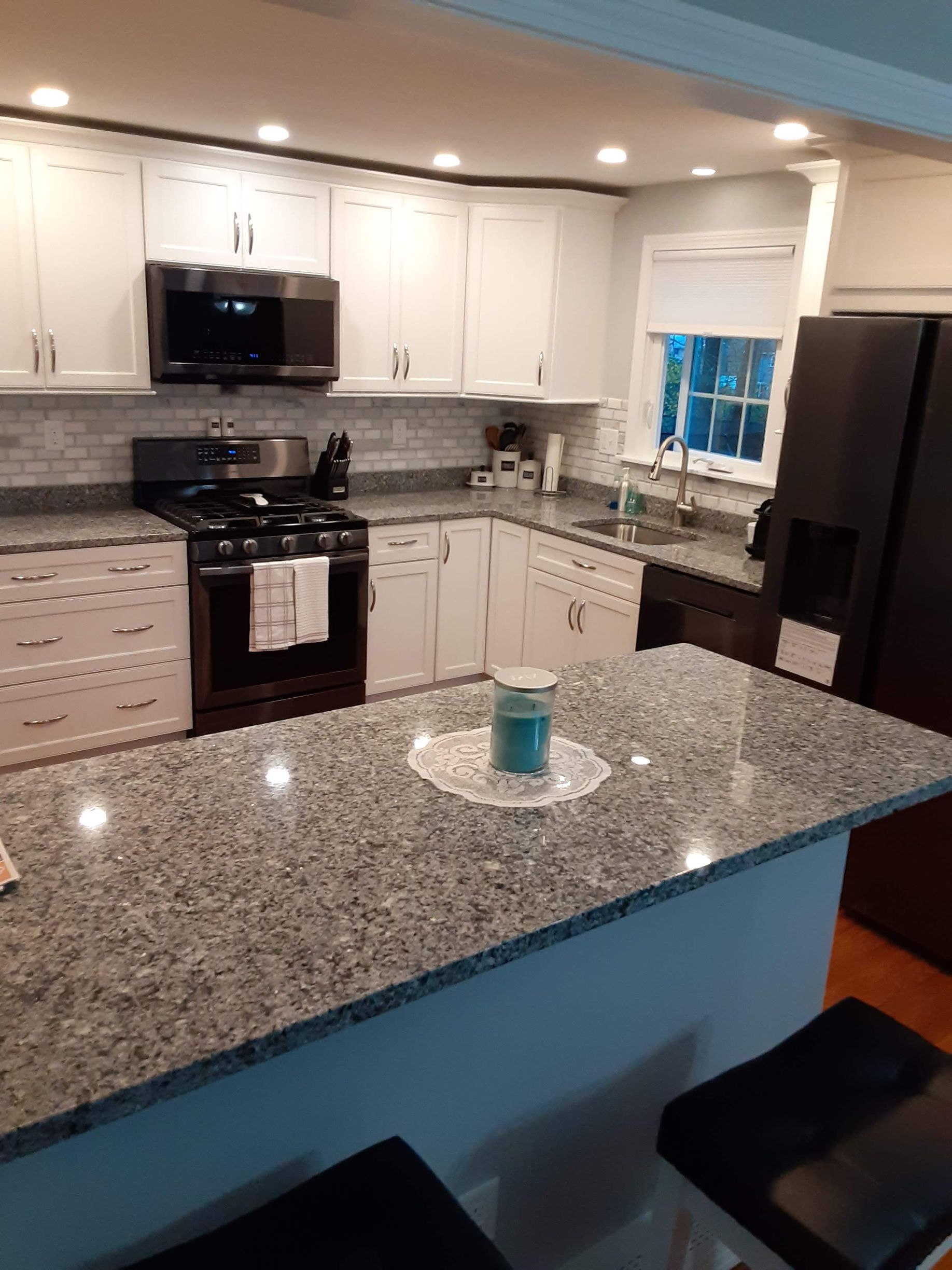 Modern kitchen with white cabinets, granite island, black appliances, and a window over the sink.