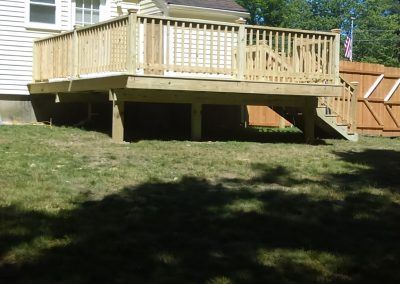 Wooden deck with railing on a sloped backyard lawn beside a house and fence