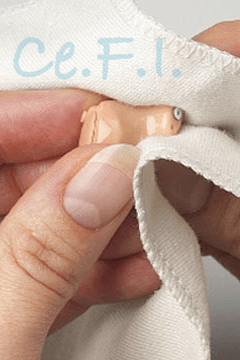 Una mano sostiene una pequeña figurita beige envuelta en papel de seda blanco, con el texto “Ce.F.” en azul claro visible.
