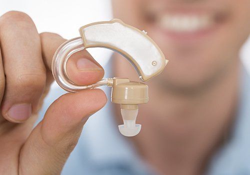 Primer plano de una mano sosteniendo un pequeño audífono o dispositivo auditivo de color beige con un molde transparente.