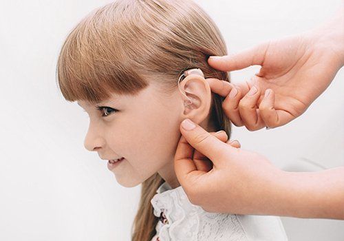 Manos ajustando un audífono infantil sobre un fondo blanco.