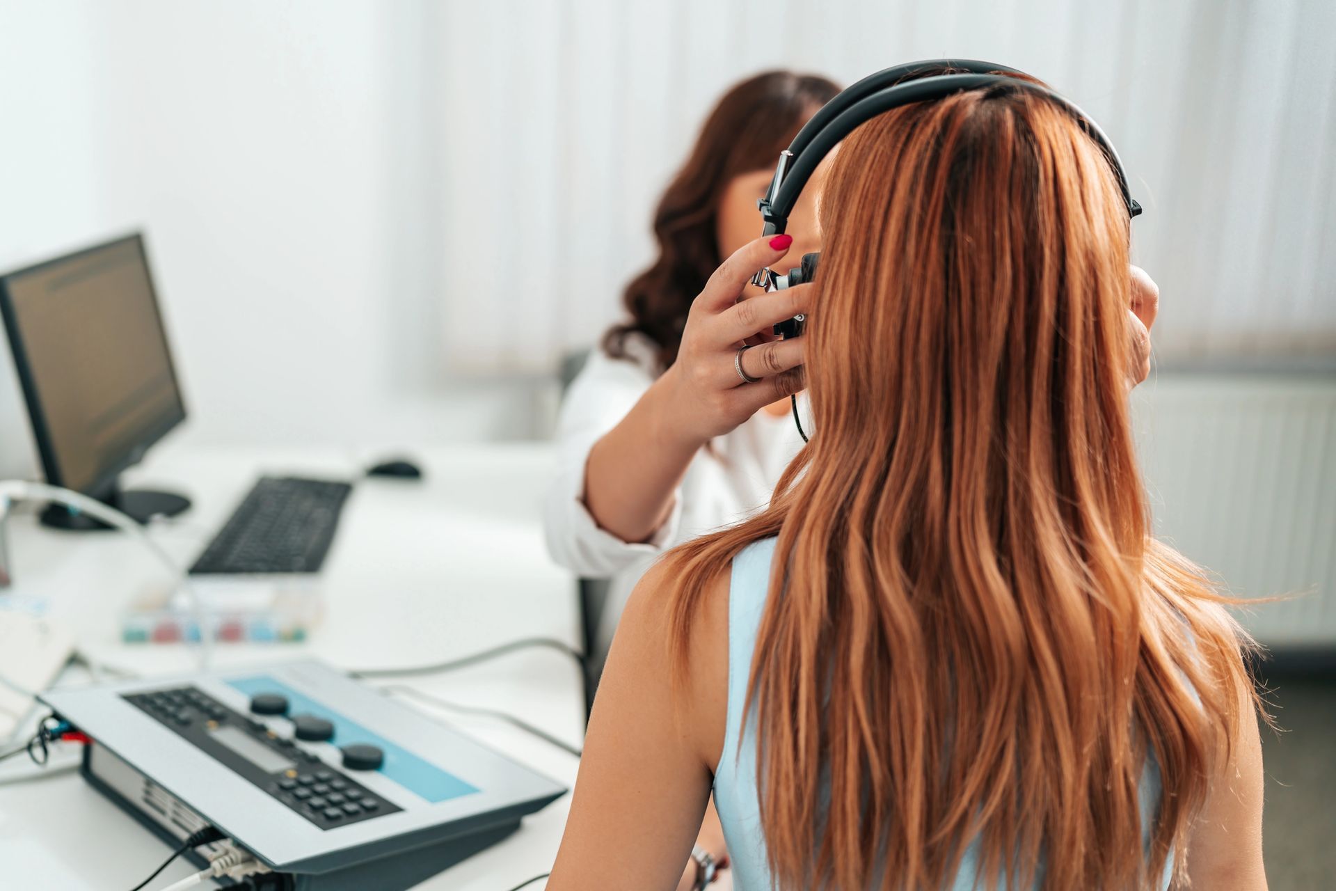 Mujer con auriculares en un escritorio con ordenador y teléfono en un entorno de oficina.