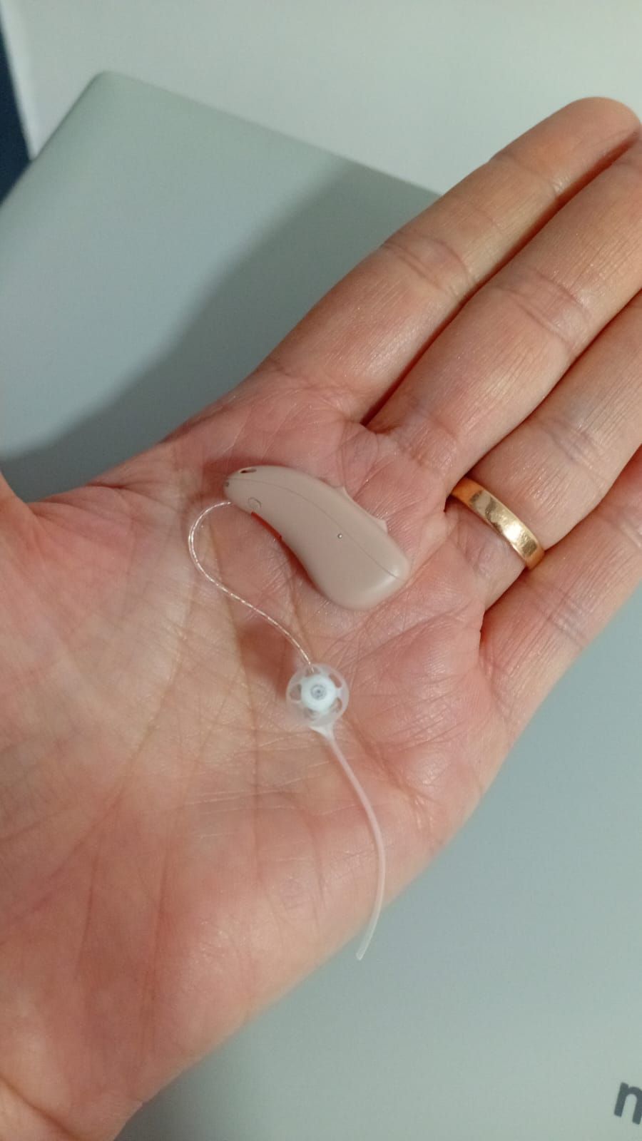 Mano sosteniendo un audífono con cable transparente y un auricular de cúpula beige.