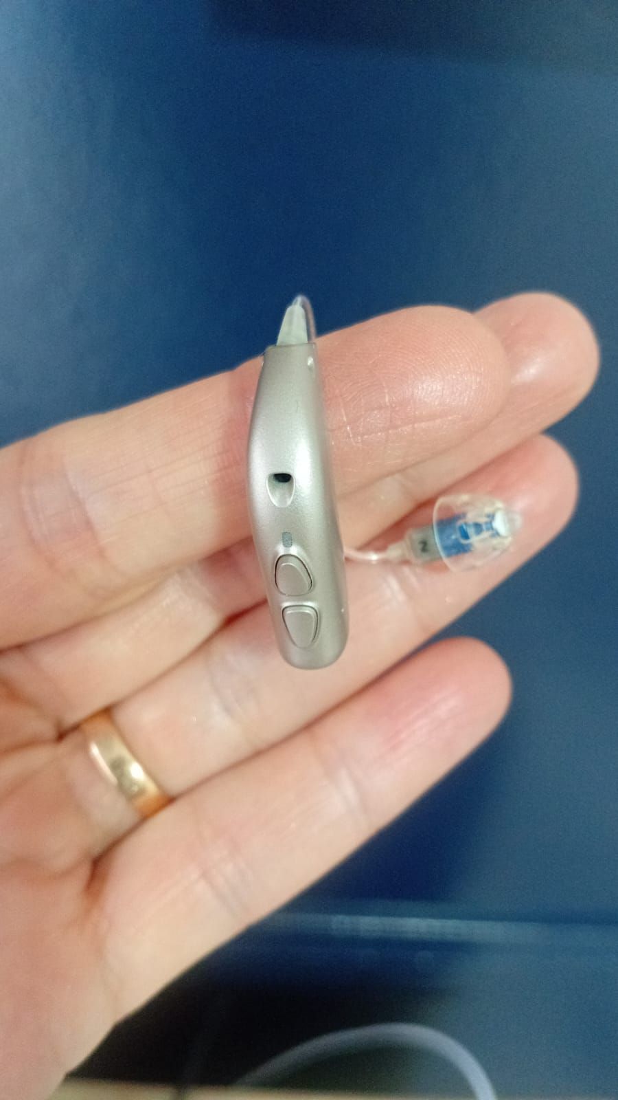 Mano sosteniendo un pequeño dispositivo de metal plateado sobre un fondo azul.