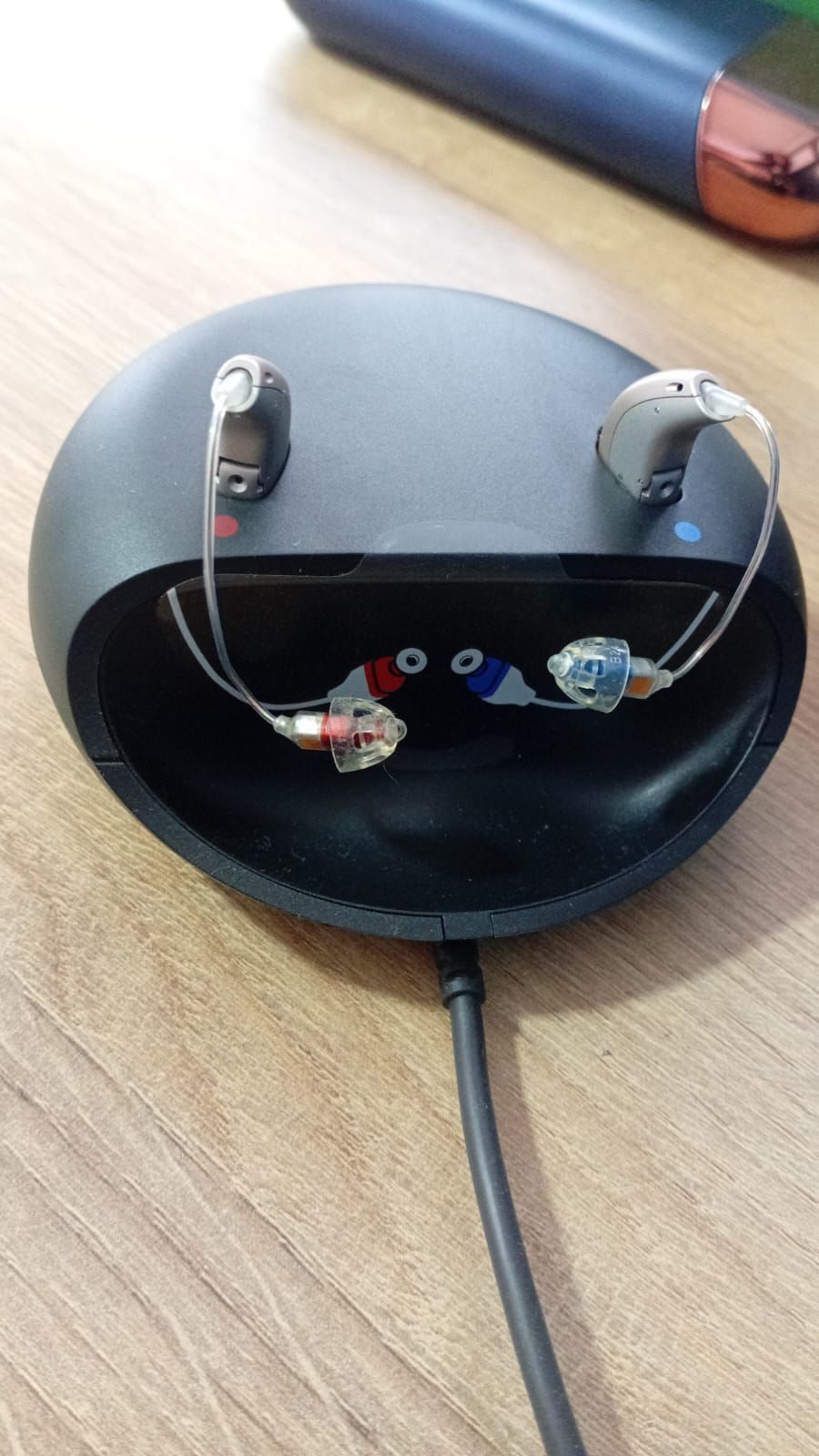 Audífono abierto que muestra los cables y componentes internos sobre una mesa de madera.