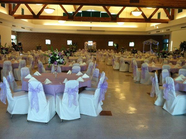 Banquet hall with round tables, white chair covers, and purple sashes set for an event