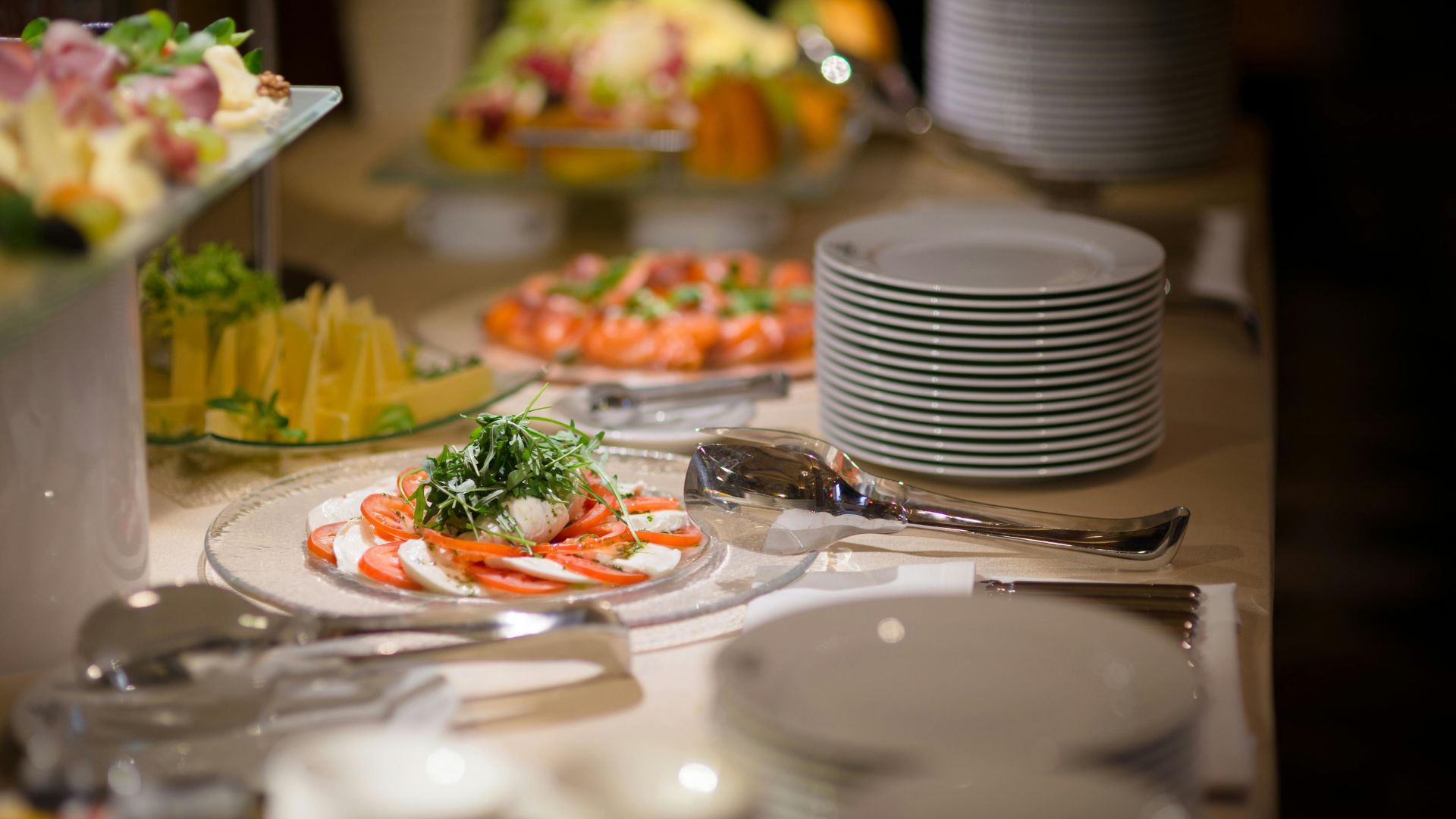 Buffet table with plated shrimp, stacked white plates, and assorted appetizers in a warm indoor setting