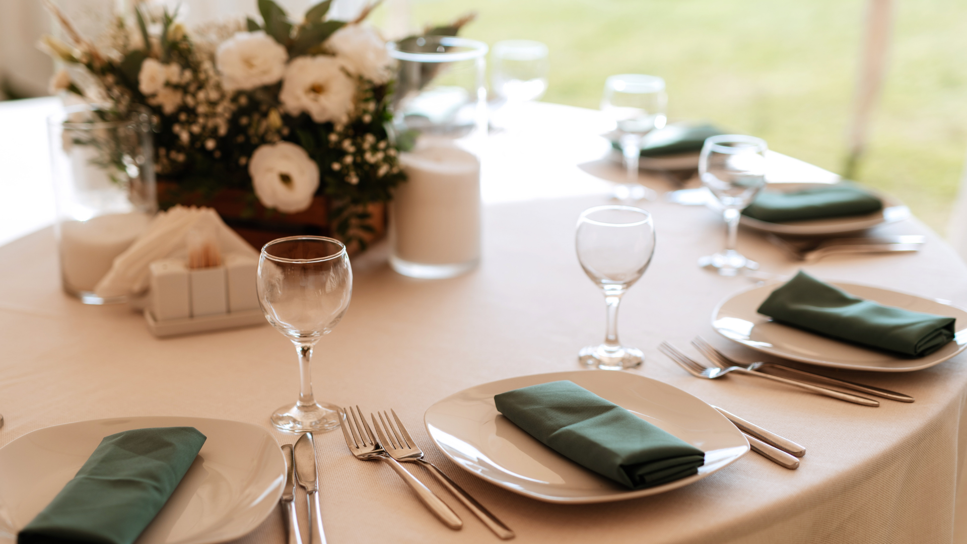 Elegant banquet table set with white plates, silverware, green napkins, wine glasses, and a floral centerpiece.