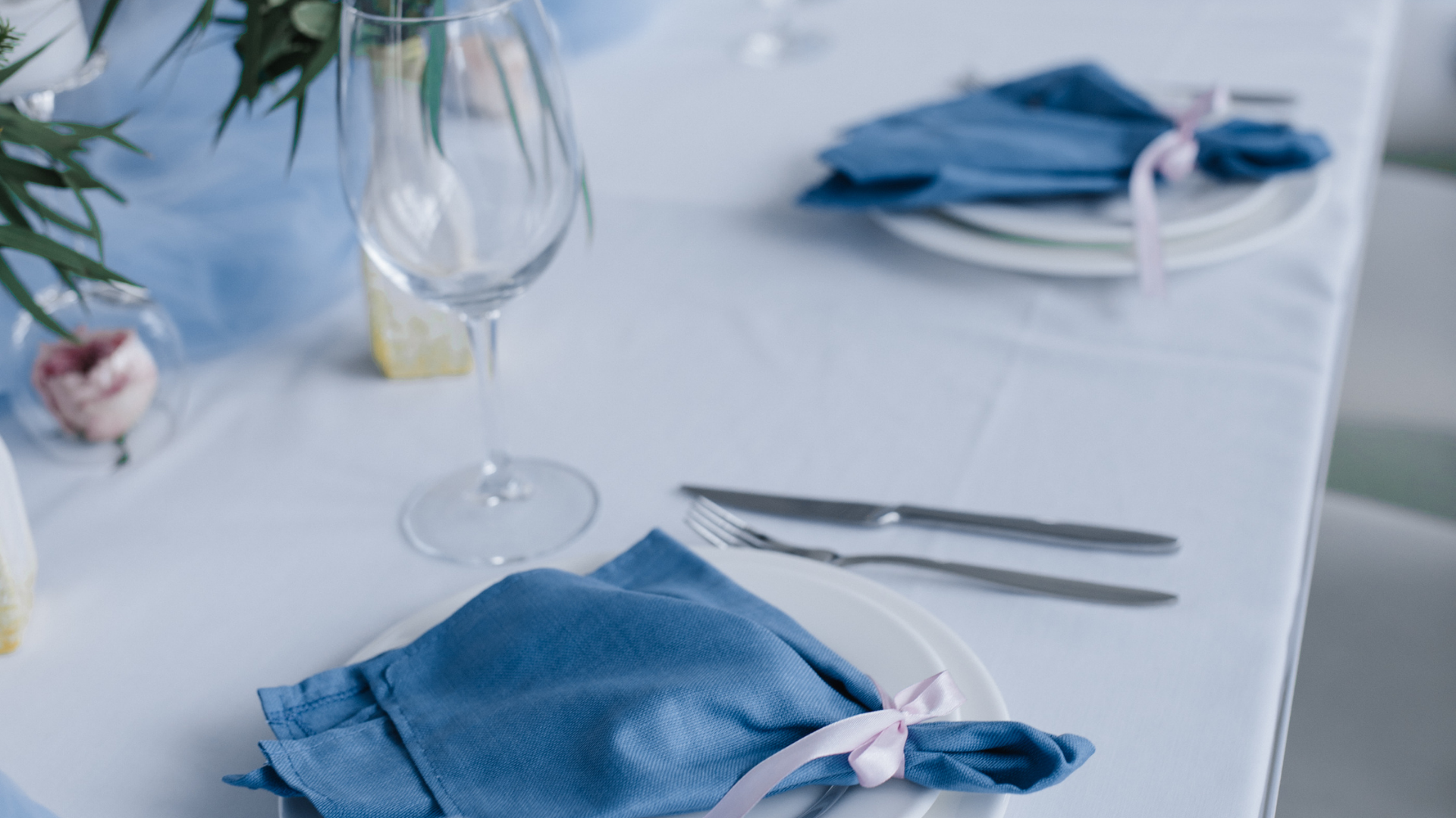 Elegant table setting with blue napkins, wine glasses, and silverware on a white tablecloth