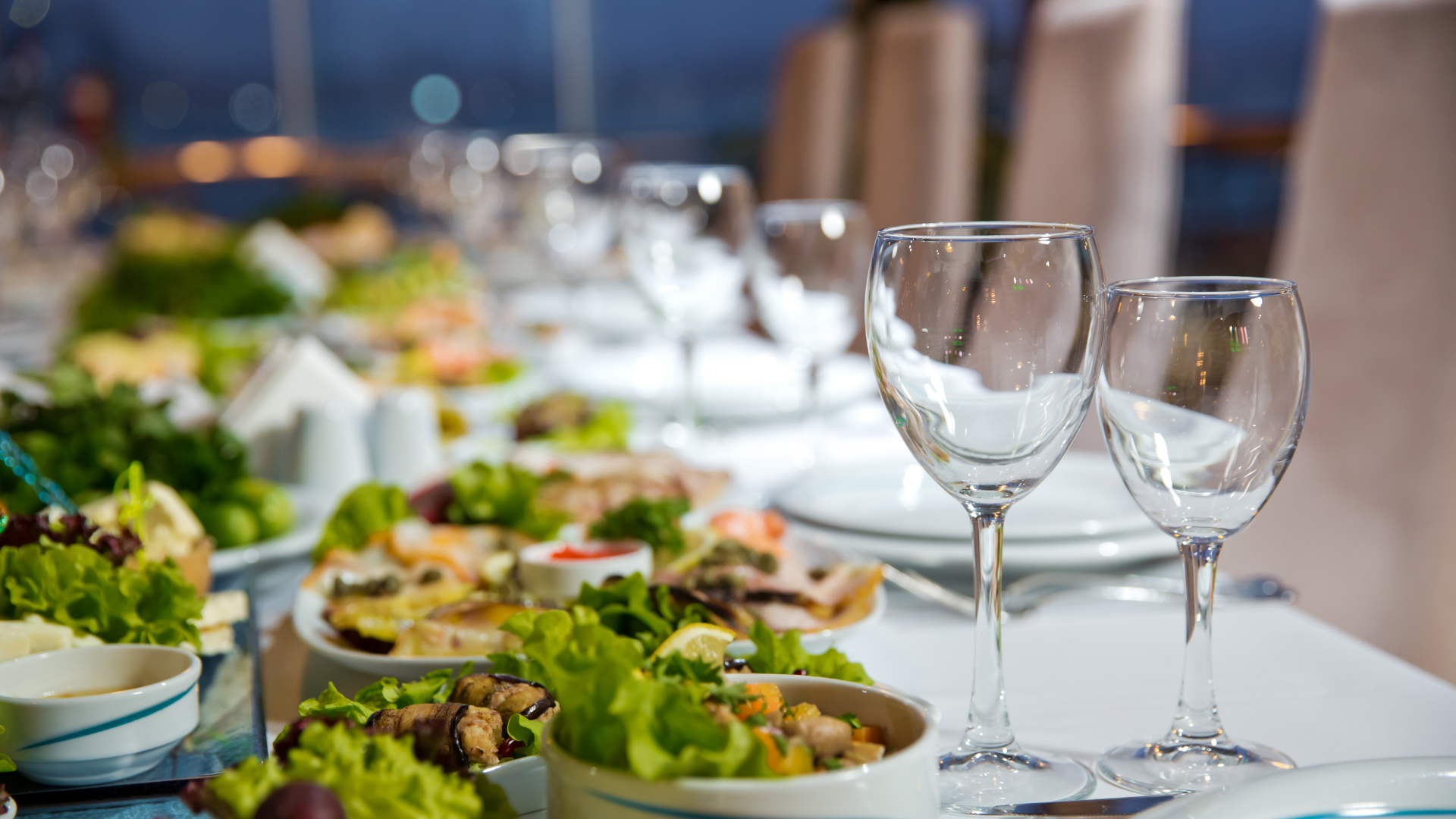 Set dining table with salads, dishes, and empty wine glasses in a bright restaurant setting