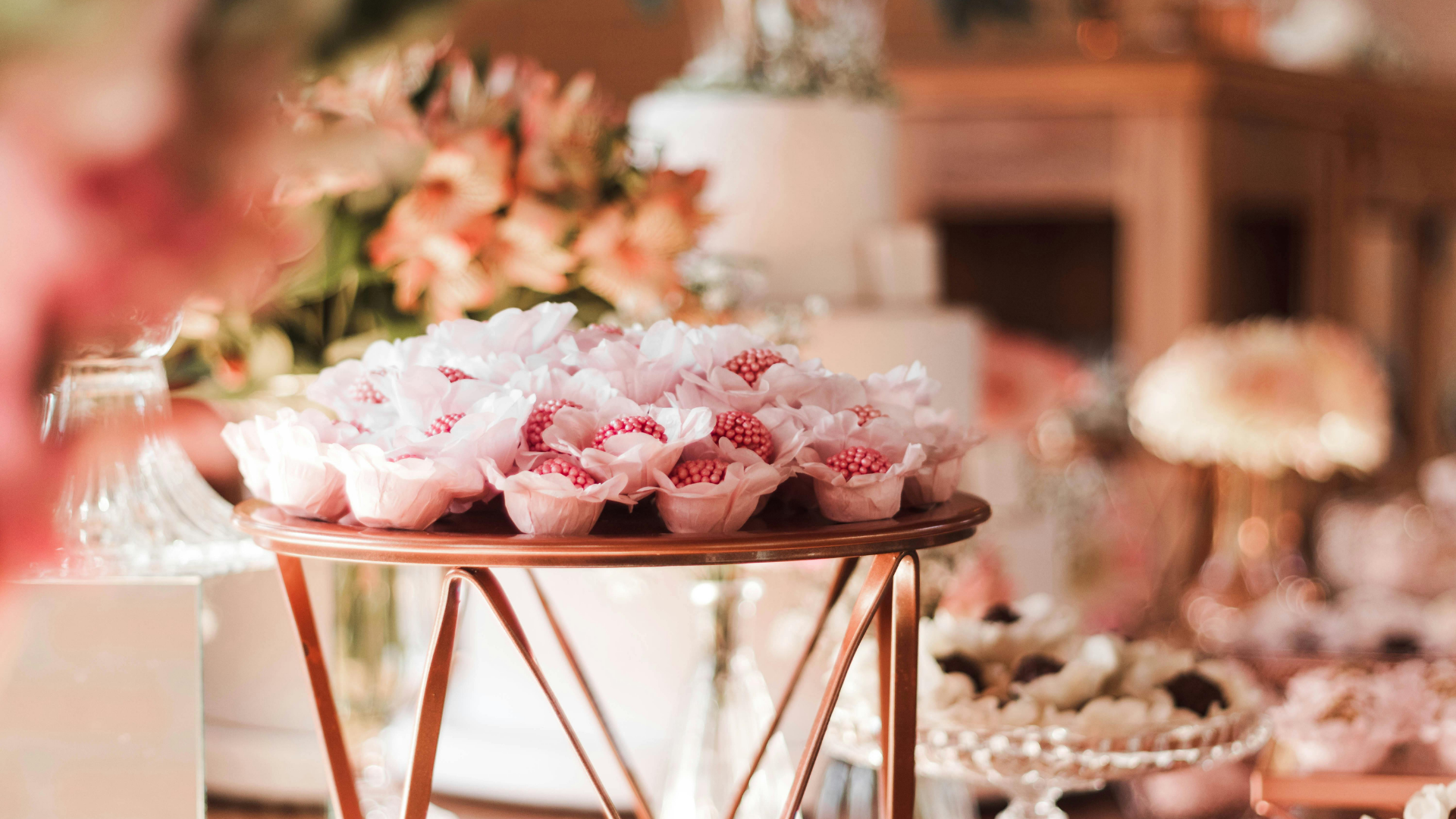 Pink and white dessert cups on a copper stand at a decorated party table