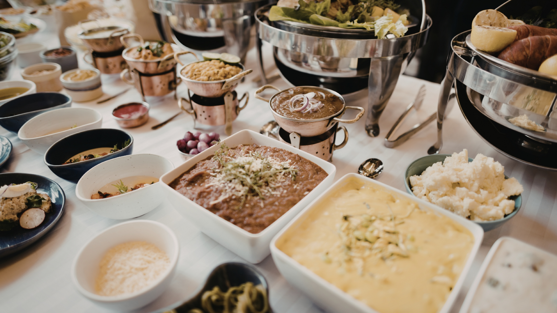 Buffet table with assorted dishes in serving bowls and pans, including creamy sauces, salads, and bread.