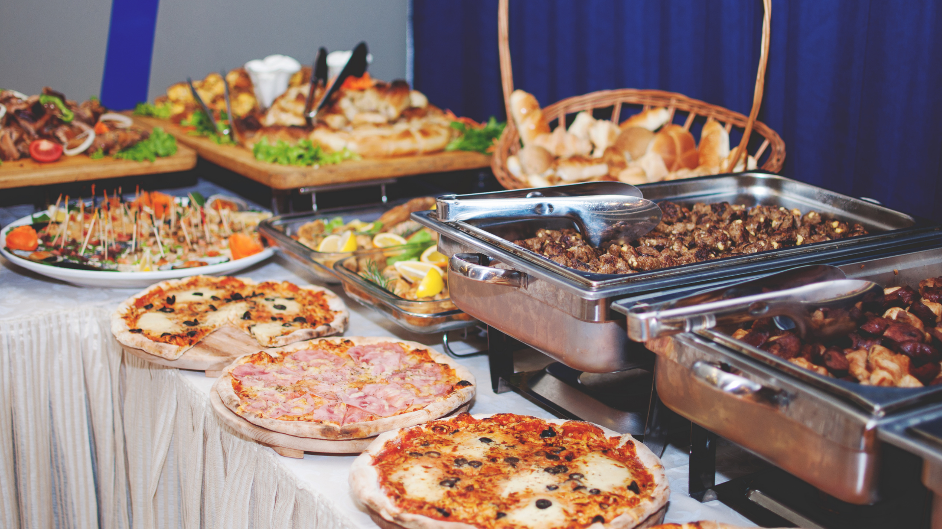 Buffet table with pizzas, trays of food, and serving dishes at an indoor event