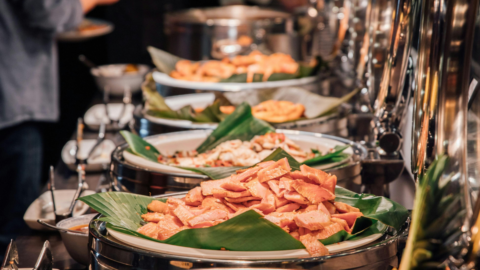 Buffet spread of grilled chicken skewers on banana leaves, served in chafing dishes